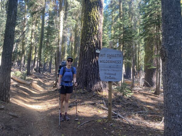 A happy guest stands next a Mt Shasta Wilderness sign on a summit hike of Mt Shasta via the Clear Creek route.
